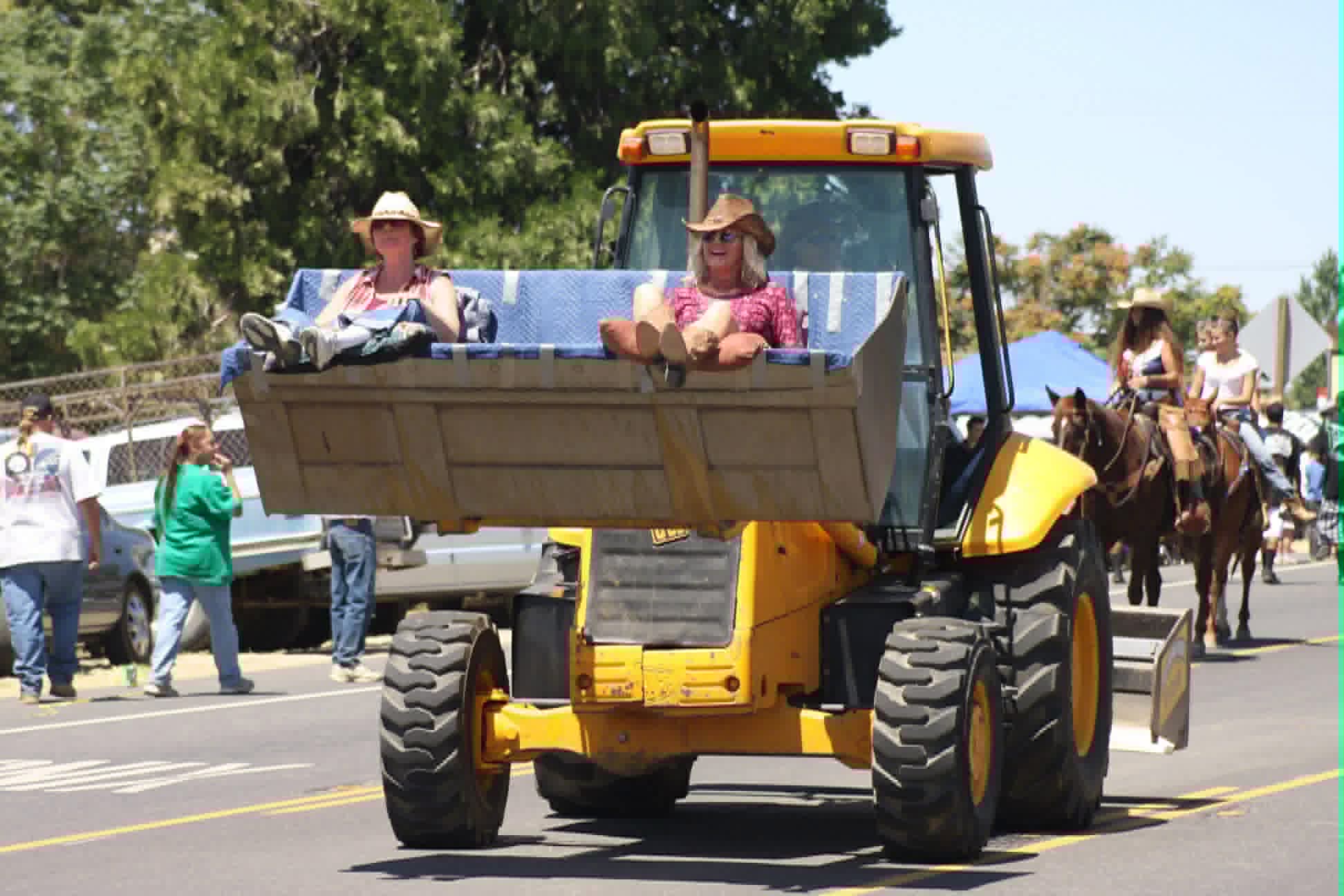 People riding in the bucket of a backhoe during the parade